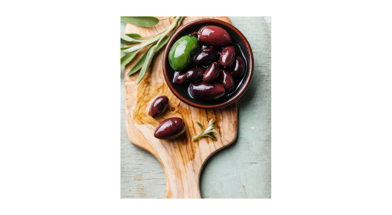 Olives on a wooden cutting board with a sprig of rosemary nearby. 